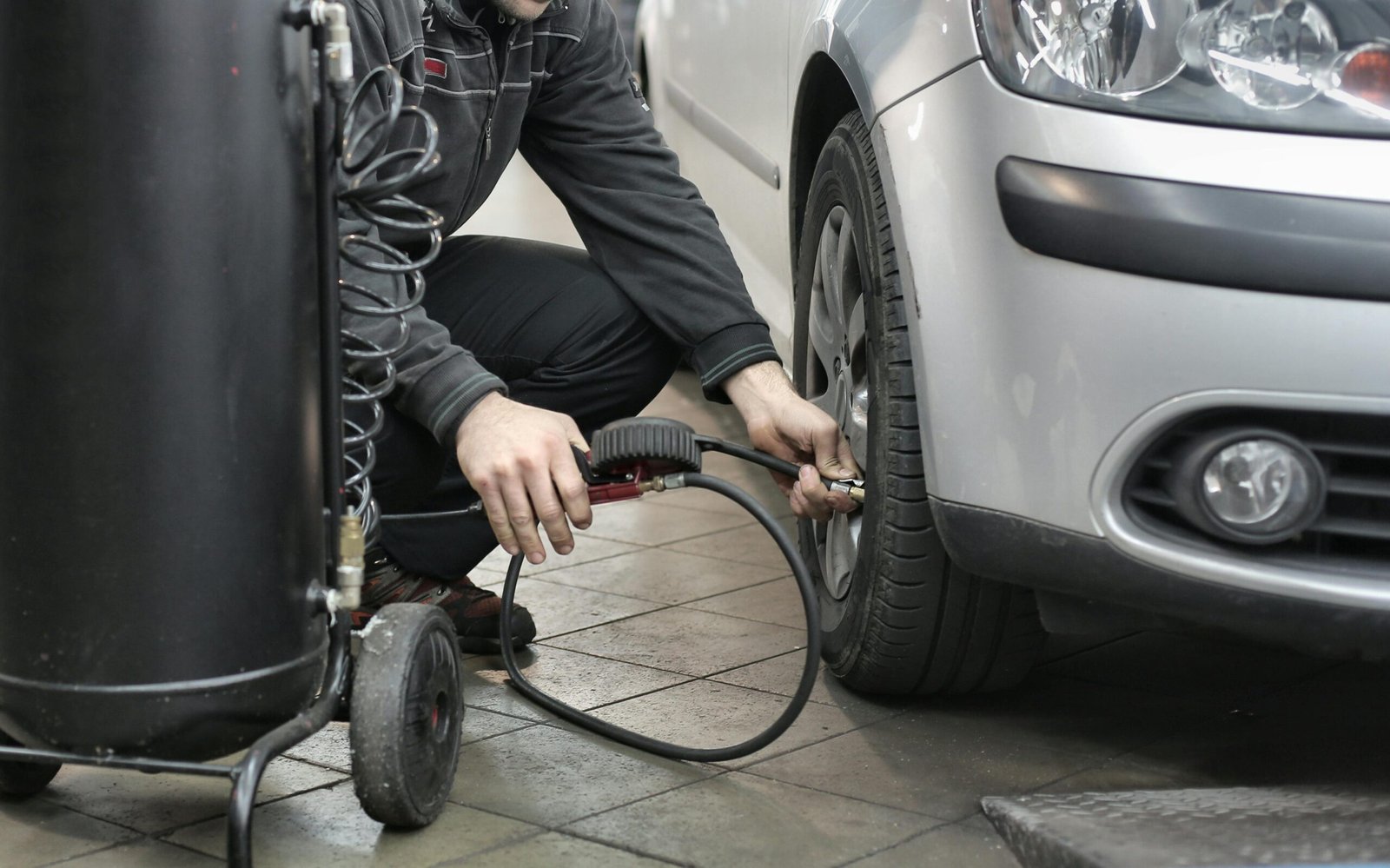 Man in black jacket and black pants sitting near silver vehicle